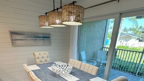A dining area with a wooden table, cushioned chairs, and a woven pendant light. - TRENDY BEACH CONDO ON THE GROUND FLOOR! (Sanibel)