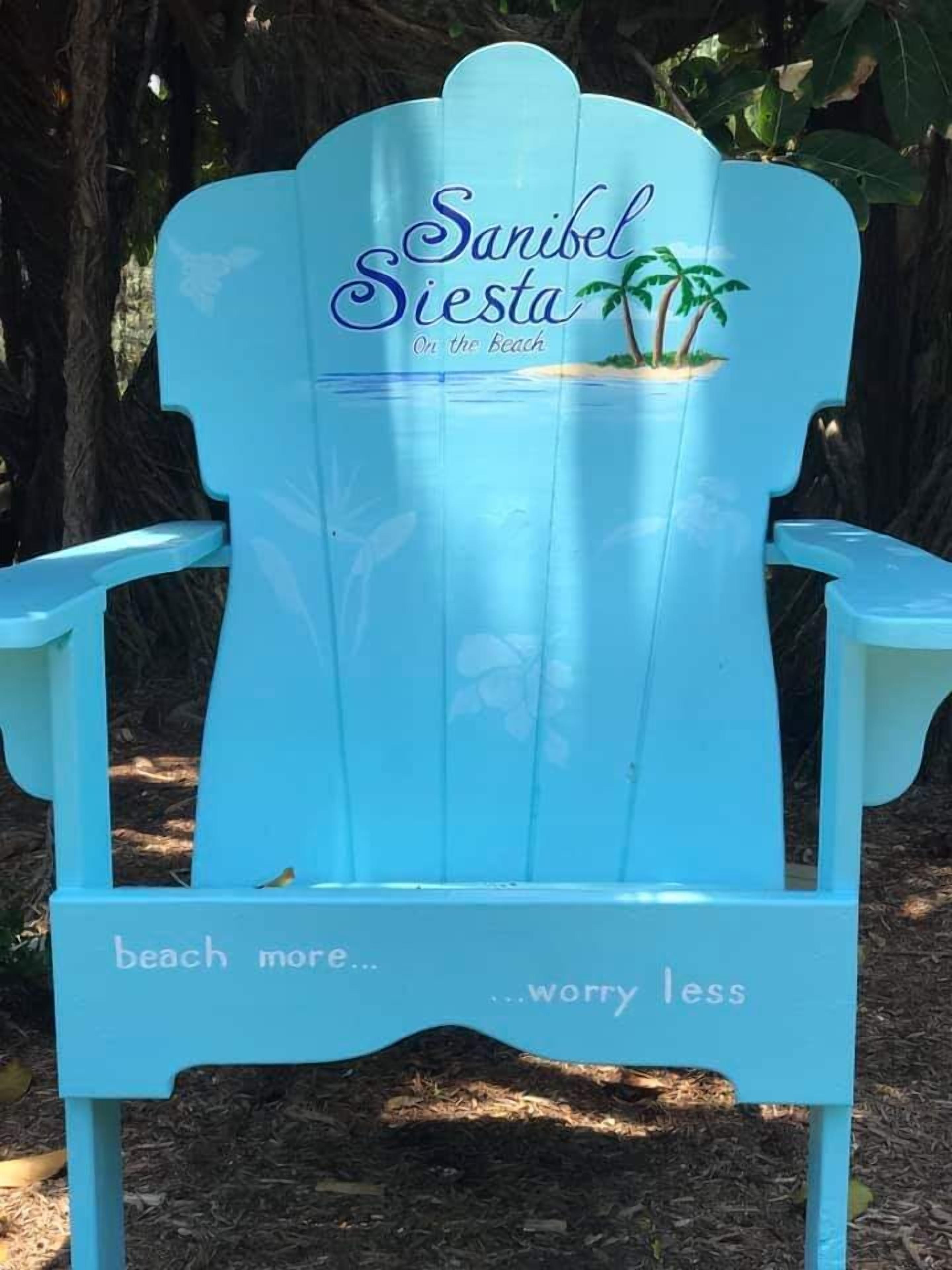 Une chaise Adirondack bleu clair, portant l’inscription « Sanibel Siesta On the Beach » et la mention « profitez davantage de la plage… et inquiétez-vous moins ».