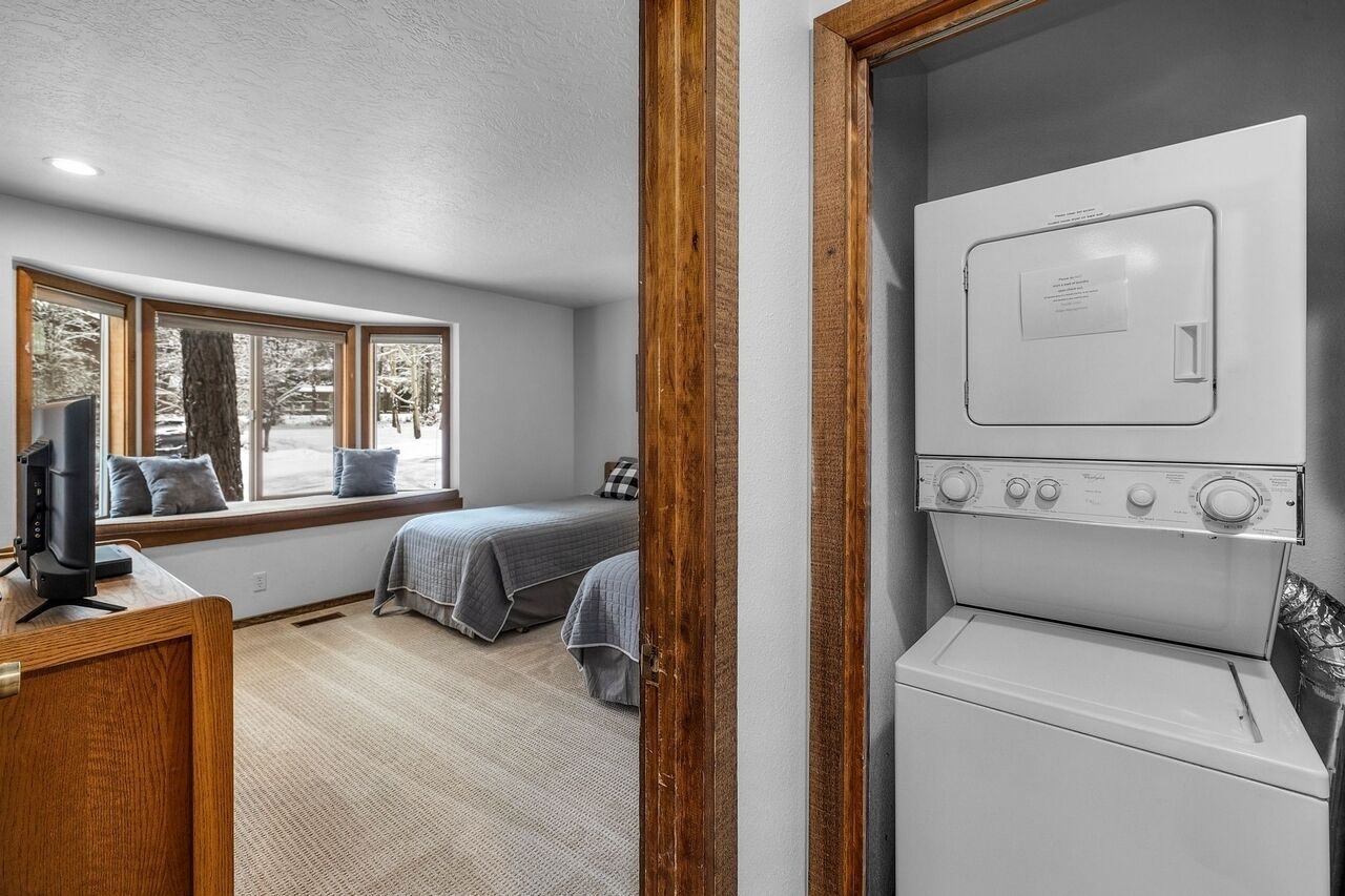 A bedroom with a large window, a washing machine, and a wooden desk.