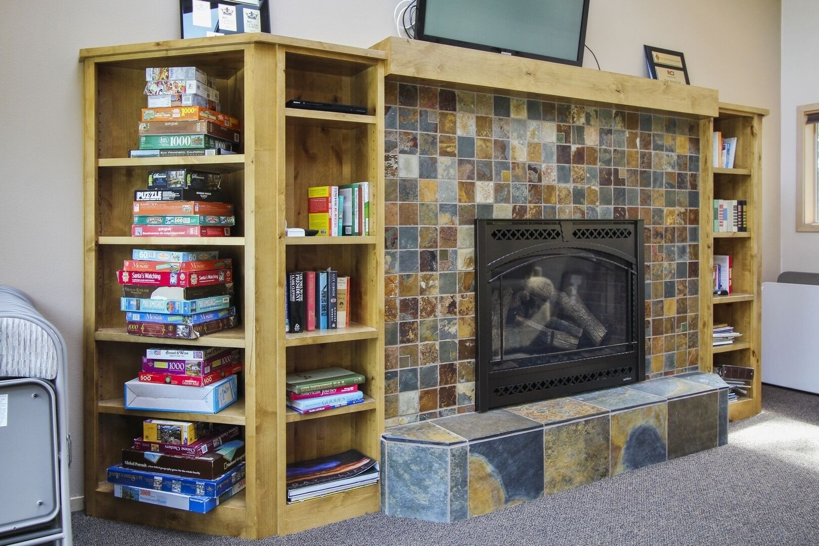 A cozy room with a fireplace, wooden bookshelves filled with books and board games, and a tiled wall.