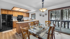 Una cocina moderna con armarios de madera, un refrigerador negro y una mesa de comedor de vidrio con sillas.