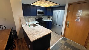 Eine kleine Küche mit dunkelblauen Schränken, einem Edelstahlkühlschrank, einer Mikrowelle und einem Waschbecken mit einer Granitarbeitsplatte.