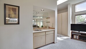 Eine kompakte Küche mit eingebautem Spülbecken, einem Weinkühlschrank aus Glas und einem Flachbildfernseher.