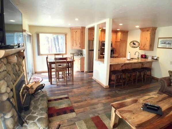 A spacious living room with a stone fireplace, a dining area, and a kitchen with wooden cabinets.