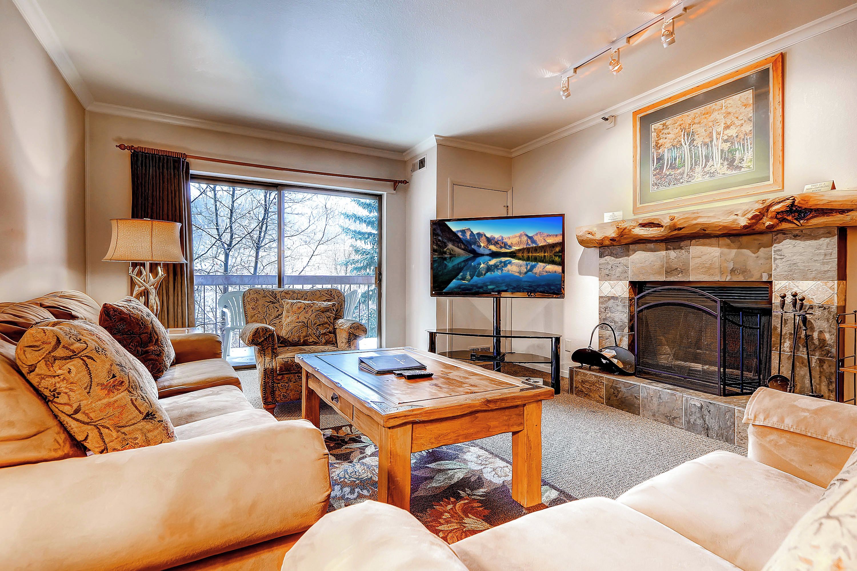 Una sala de estar con chimenea, televisor y un ventanal con vista a árboles.