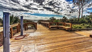 En træterrasse med bænke og en haveslange, der fører til udsigt over havet under en overskyet himmel.