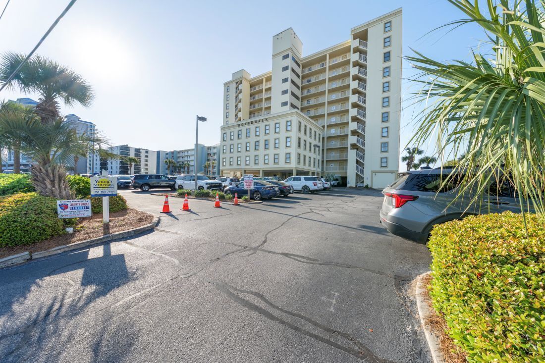 A parking lot with several cars, a building with multiple floors, and palm trees.