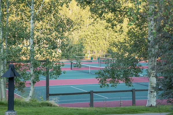 Una cancha de tenis al aire libre rodeada de árboles.