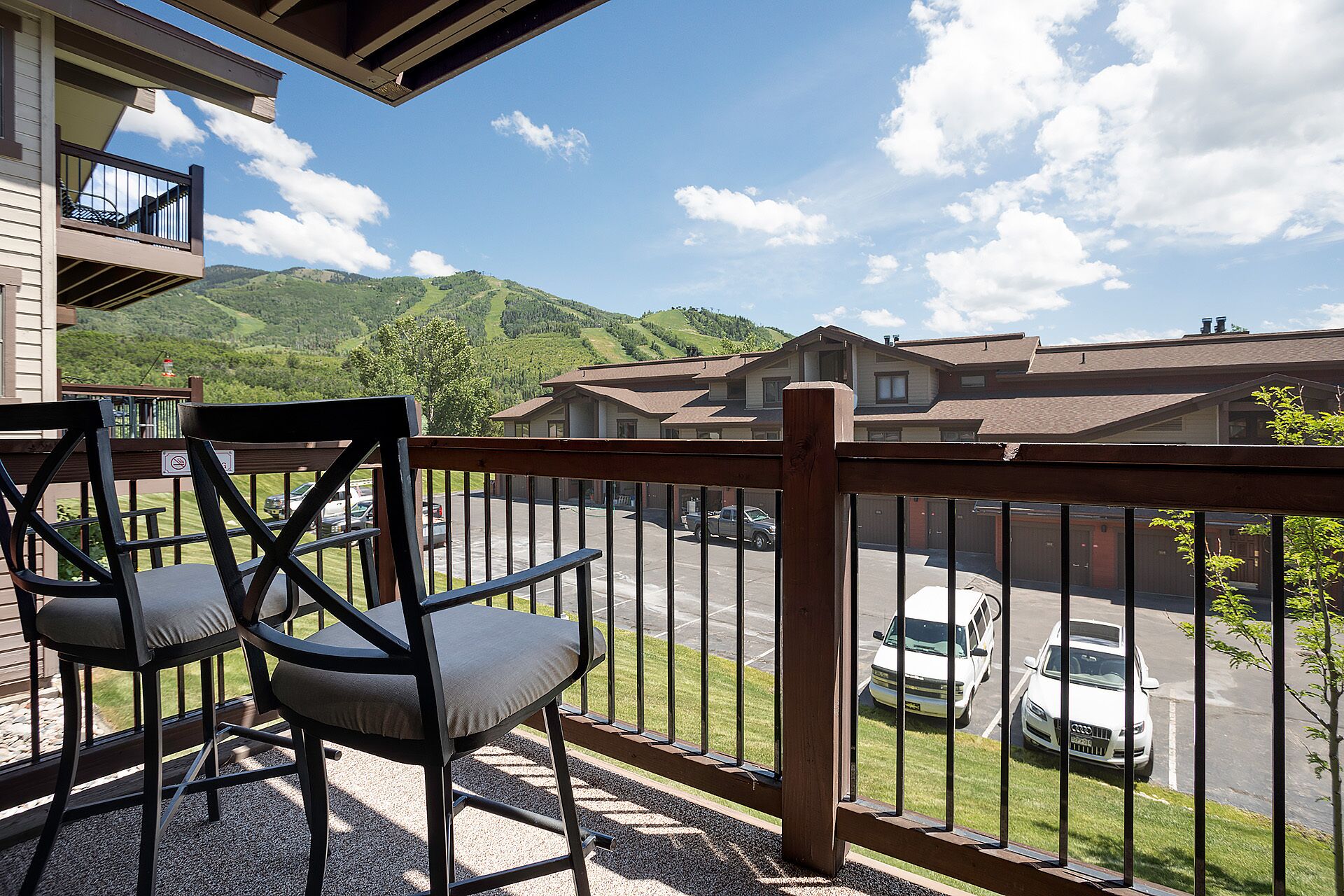 A balcony with a view of a parking lot and houses, a chair, and a railing.