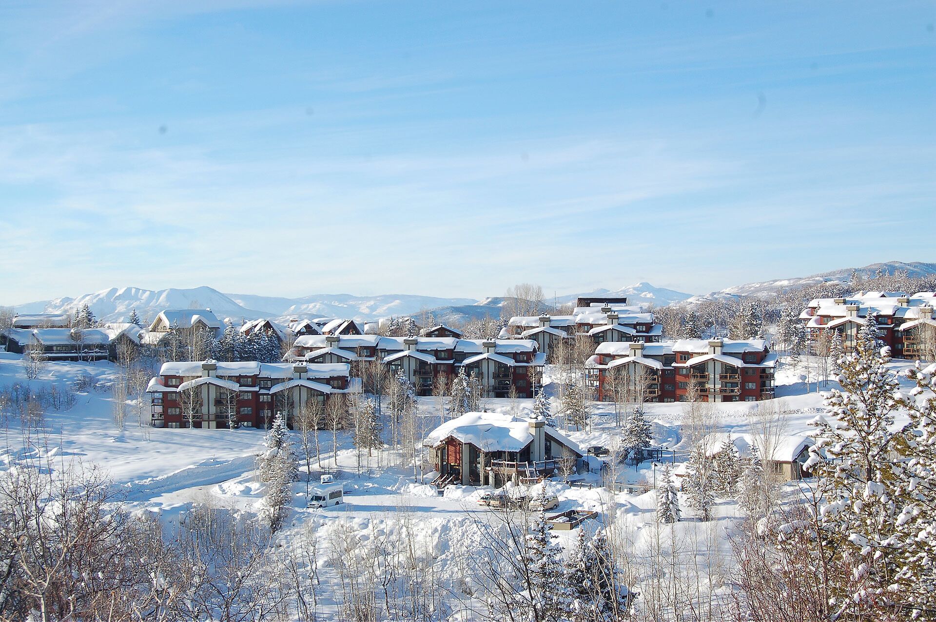 A snow-covered resort with multiple chalet-style buildings, a ski slope in the background, and a clear sky.