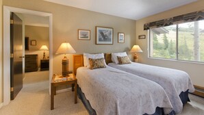 A bedroom with two beds, a window with a view of trees, and a door leading to another room.