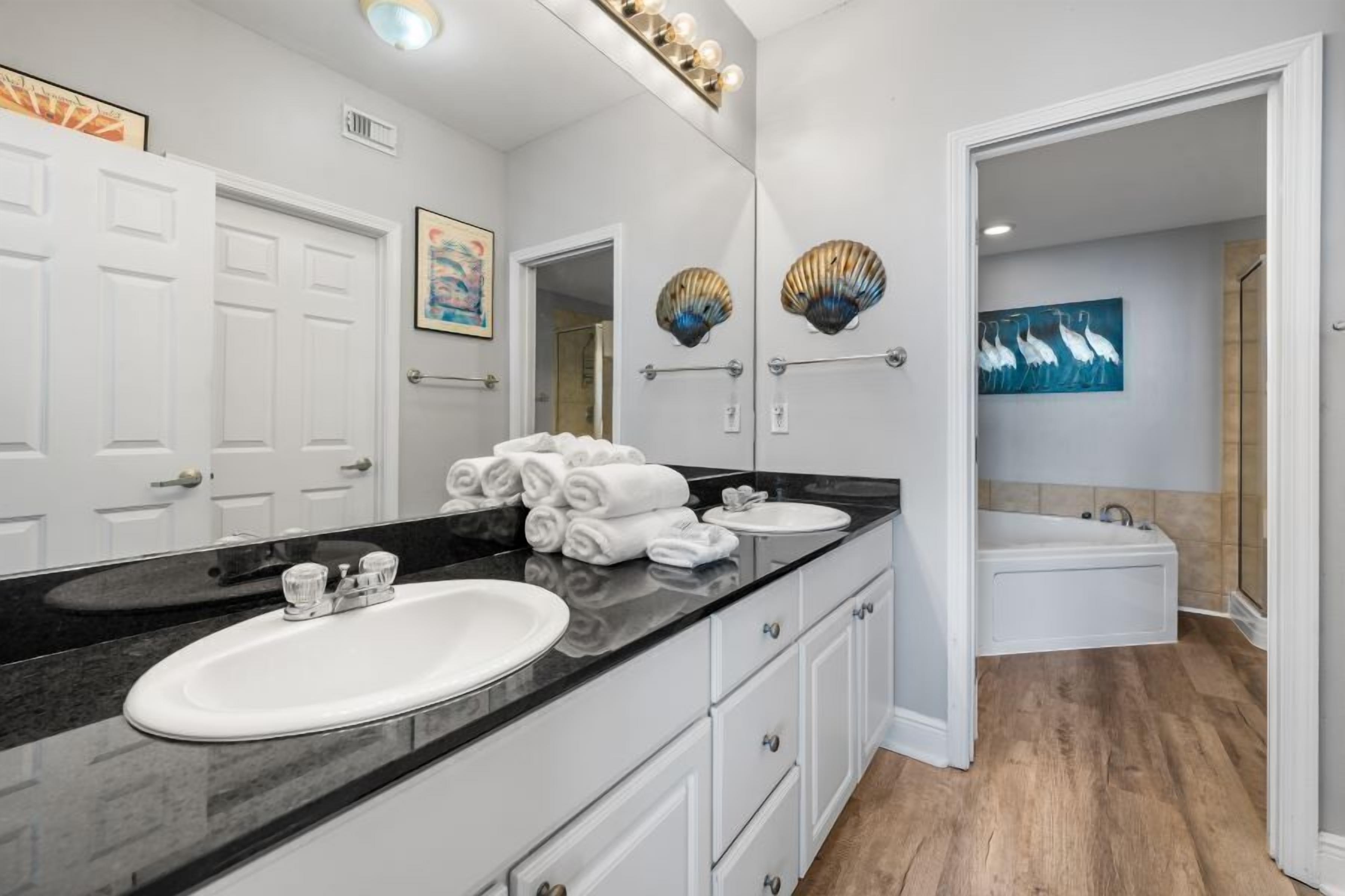 A modern bathroom with a black countertop, white sink, and a large mirror. There are two white towel racks and a painting on the wall.