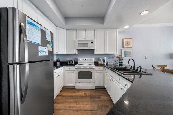 A modern kitchen with white cabinets, stainless steel appliances, and a wooden floor. - Spacious Beachfront Condo w/ Sunset Views of the Gulf | Pool & Sauna | Sleeps 8 (Gulf Shores)