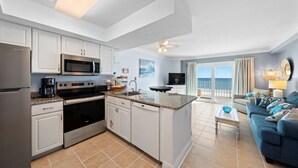 Una cucina moderna con mobili bianchi, elettrodomestici in acciaio inossidabile e una grande isola. C'è un'area pranzo con un divano blu e vista sull'oceano attraverso ampie finestre.