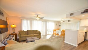 A spacious living area with a large sofa, a coffee table, and a dining table with chairs. There are ceiling fans and a kitchen area visible in the background. - Thunder Island 61B-Baywater 39th St, Free WiFi, Pool, Elev, W/D, AC (Ocean City)