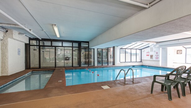 An indoor swimming pool with clear glass walls, a tiled floor, and a few plastic chairs. - Oak Square 109 is a spacious condo with private balcony in downtown (Gatlinburg)