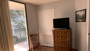 A room with a wooden dresser, a television on top, a chair, and a sliding glass door leading to a balcony. - Oak Square 109 is a spacious condo with private balcony in downtown (Gatlinburg)