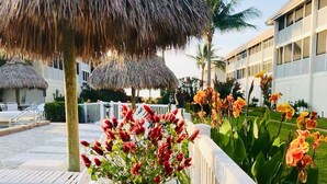 A poolside area with lounge chairs, a thatched umbrella, and flower arrangements. - Flip Flop Fun (Sanibel)
