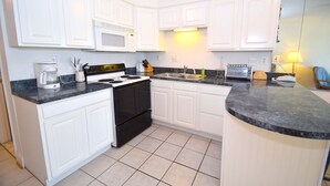 A kitchen with white cabinets, a black stove, a microwave, and a sink.