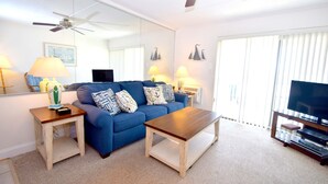 A living room with a blue sofa, wooden coffee table, and a TV stand with a flat-screen TV.
