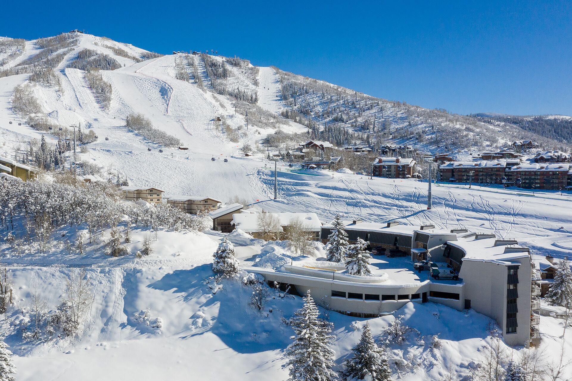 A snow-covered mountain with ski slopes and a resort area including buildings and a parking area.