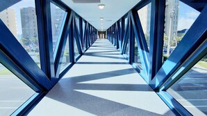 A covered pedestrian walkway with glass panels and metal beams, leading to a building entrance. - 18th Floor Corner Condo w/ Panoramic Gulf and Lagoon Views | Sleeps 6 (Gulf Shores)