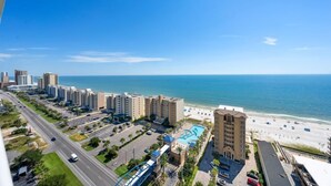 A coastal hotel with a swimming pool, beachfront view, and multiple high-rise buildings in the background. - 18th Floor Corner Condo w/ Panoramic Gulf and Lagoon Views | Sleeps 6 (Gulf Shores)