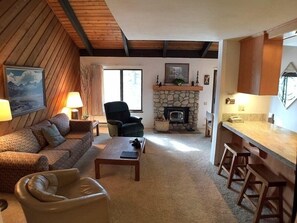 Cozy living room with a fireplace, comfortable seating, and a kitchen area.