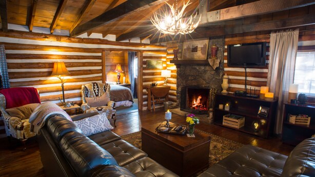 Interior de una cabaña de troncos con chimenea, sofás de cuero, pisos de madera y un televisor.