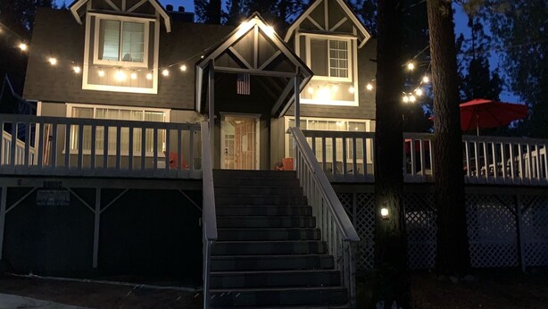 A two-story house with a front porch, a staircase leading to the entrance, and a covered area with red umbrellas.