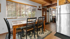 A wooden dining table with chairs, a refrigerator, and a window with blinds.