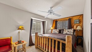 A cozy bedroom with a wooden bed, a red chair, a small table, and a ceiling fan.