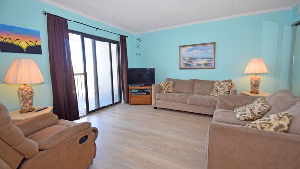 Un salon comprenant un canapé, deux fauteuils, un téléviseur posé sur un meuble en bois et un tableau accroché au mur.