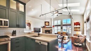 A modern kitchen with a dishwasher, stove, and microwave. There is a dining area with a sofa and a table.