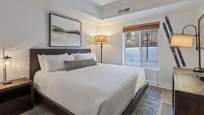 A bedroom with a large bed, a nightstand, a lamp, a window with a view of the outside, and a ski rack. - Walk to Main Street/Town Lift I Hot Tub I Sauna I Managed by Park City Lodging (PARK CITY)