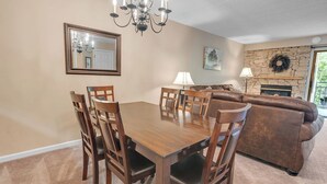 Un comedor con una mesa y sillas de madera, una chimenea y una sala de estar con un sofá y una pared de piedra.