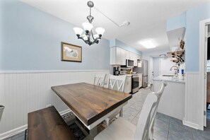 Un comedor con una mesa y sillas de madera, una araña y una cocina al fondo.