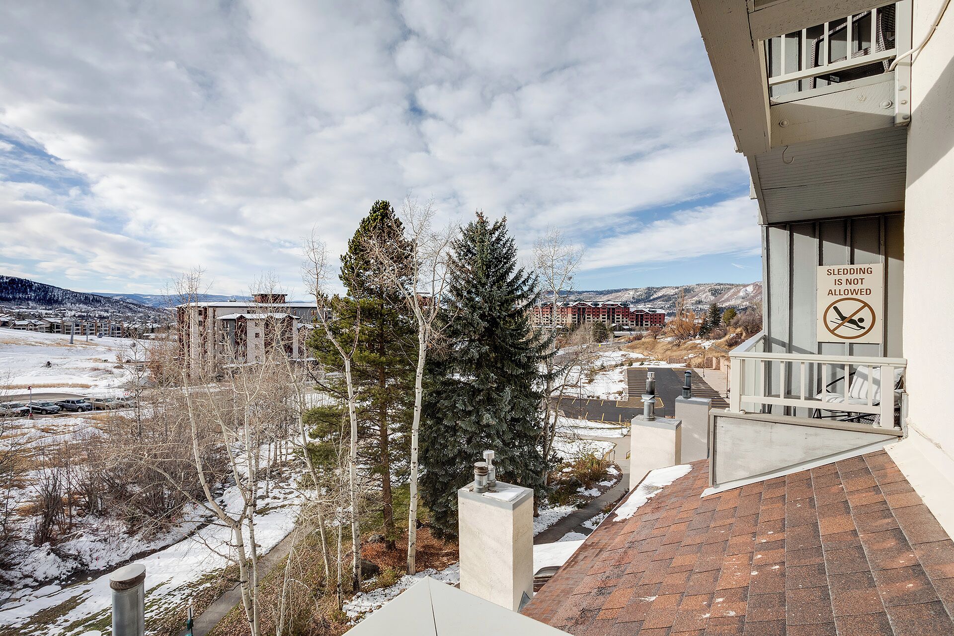 This private balcony overlooks a peaceful winter landscape, where snow-dusted hills meet evergreen trees and distant mountains create a serene mountain-town backdrop.