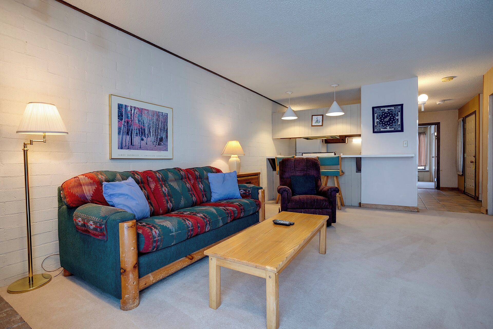 A cozy living room with a sofa, armchair, and a coffee table. There is a painting on the wall and a lamp on the floor.