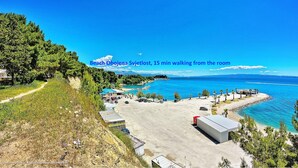 Une chambre avec vue sur la plage, donnant sur un sentier menant à la plage, un espace de stationnement et un petit bâtiment.