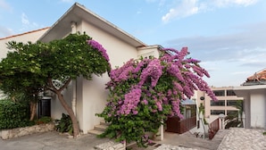 Un bâtiment doté d’un escalier en pierre menant à une porte, le tout entouré de verdure et de fleurs violettes.