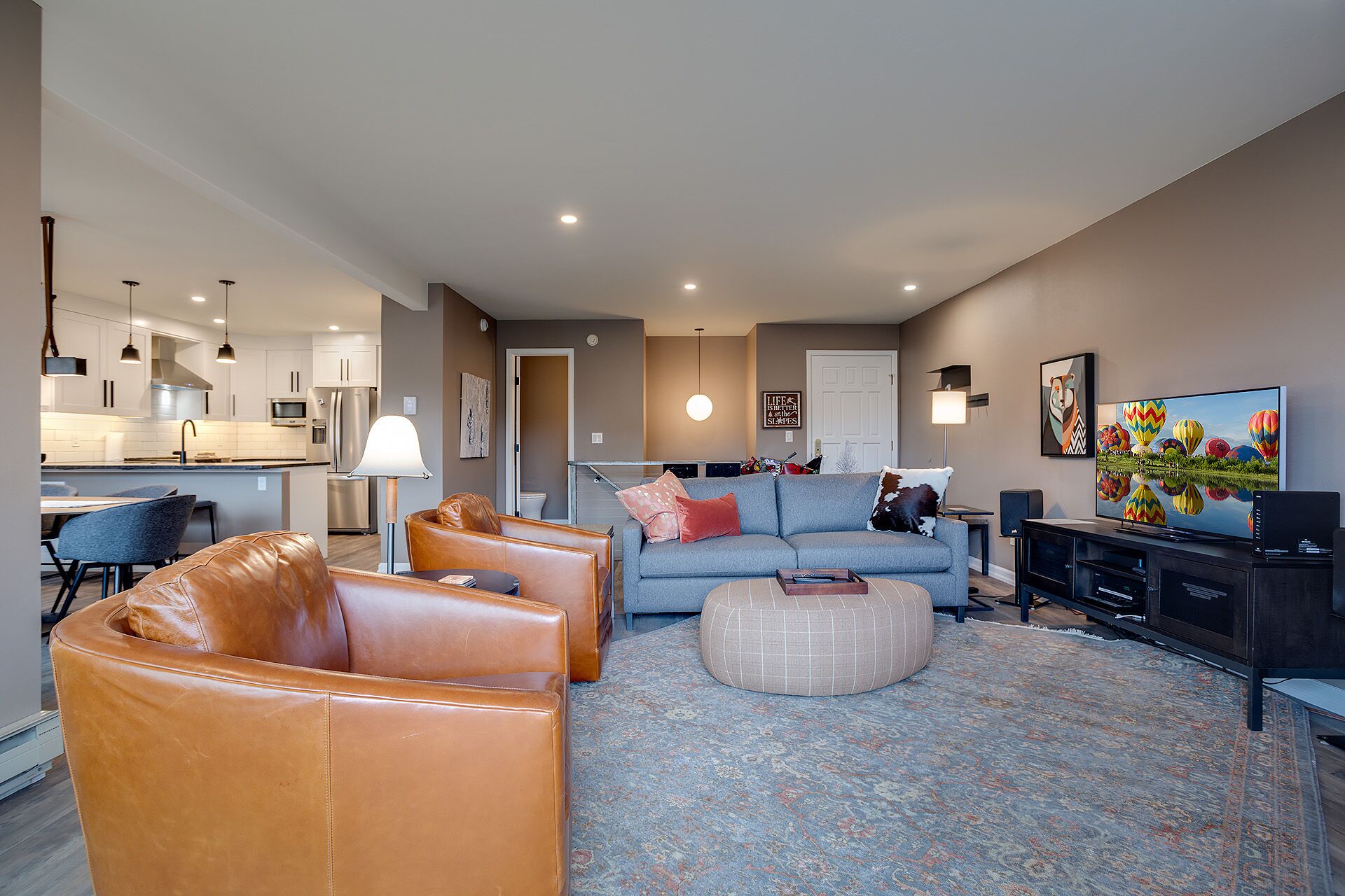 A modern living room with a sofa, ottoman, and leather chairs. There is a television, a coffee table, and a rug.