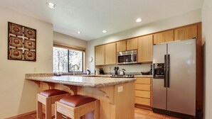 A kitchen with wooden cabinets, a stainless steel refrigerator, a microwave, and a large island with stools. - The Ridge at Sunriver - Condo #45 - Access provided to onsite seasonal swimming pool & tennis facilities, year-round hot tub plus 4 bikes (Sunriver)