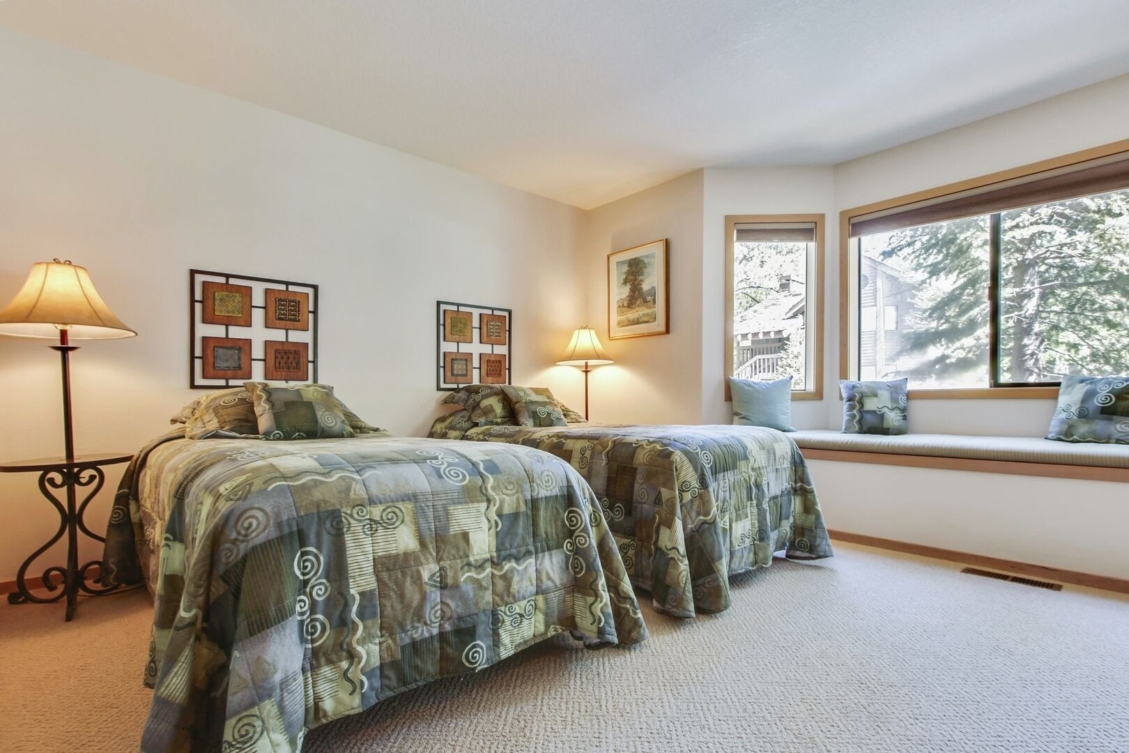 A bedroom with two beds, a window seat, and wall art.