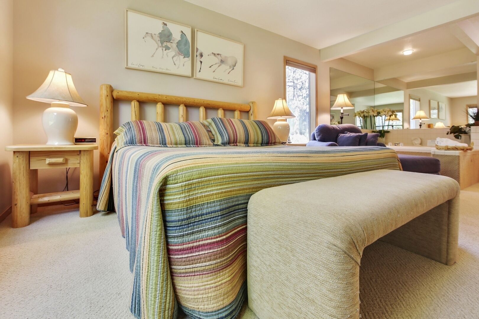 A bedroom with a bed, bedside tables, a bench, a mirror, and artwork on the wall.