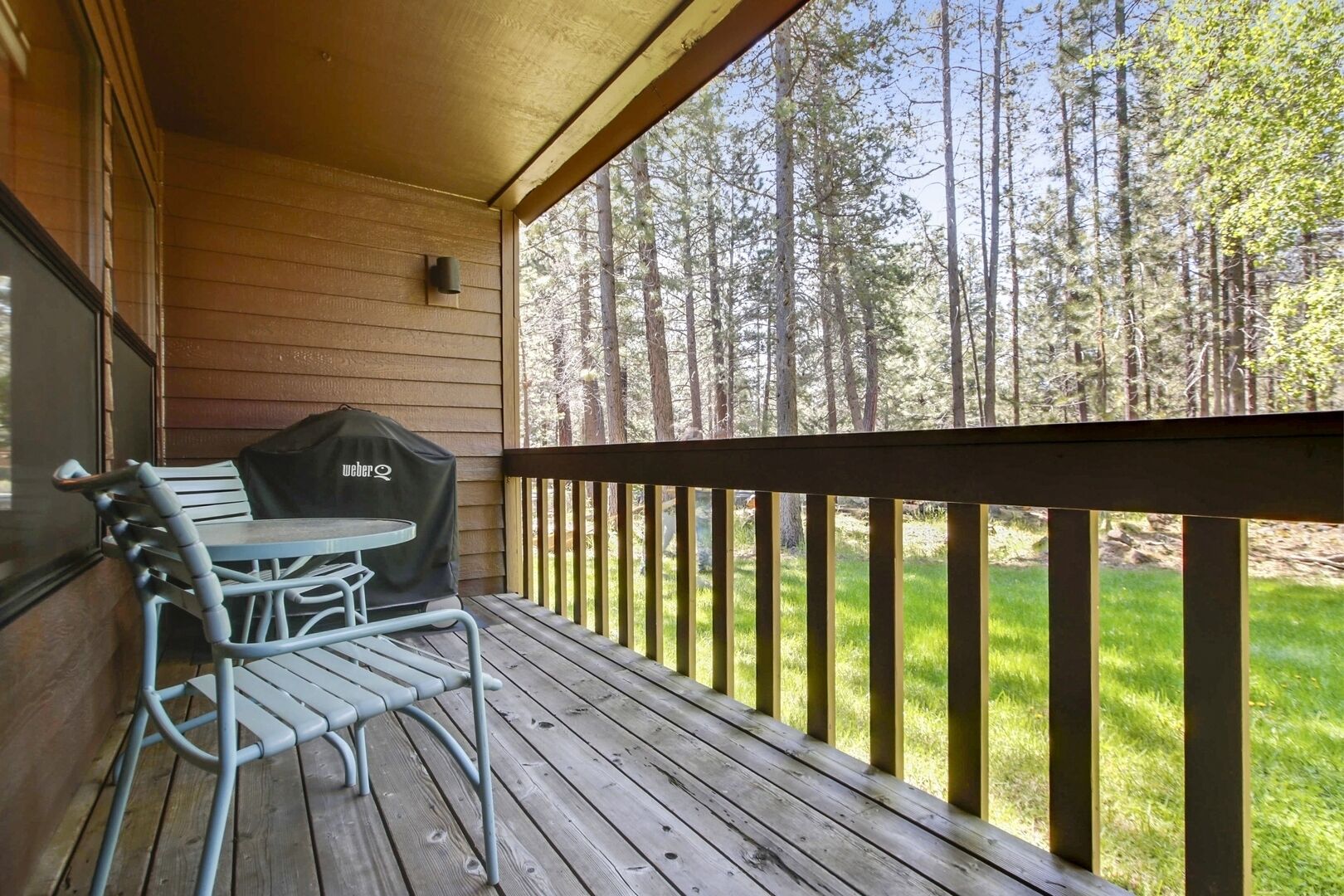 Een houten terras met een tafel, stoelen, een barbecue en uitzicht op een bos.