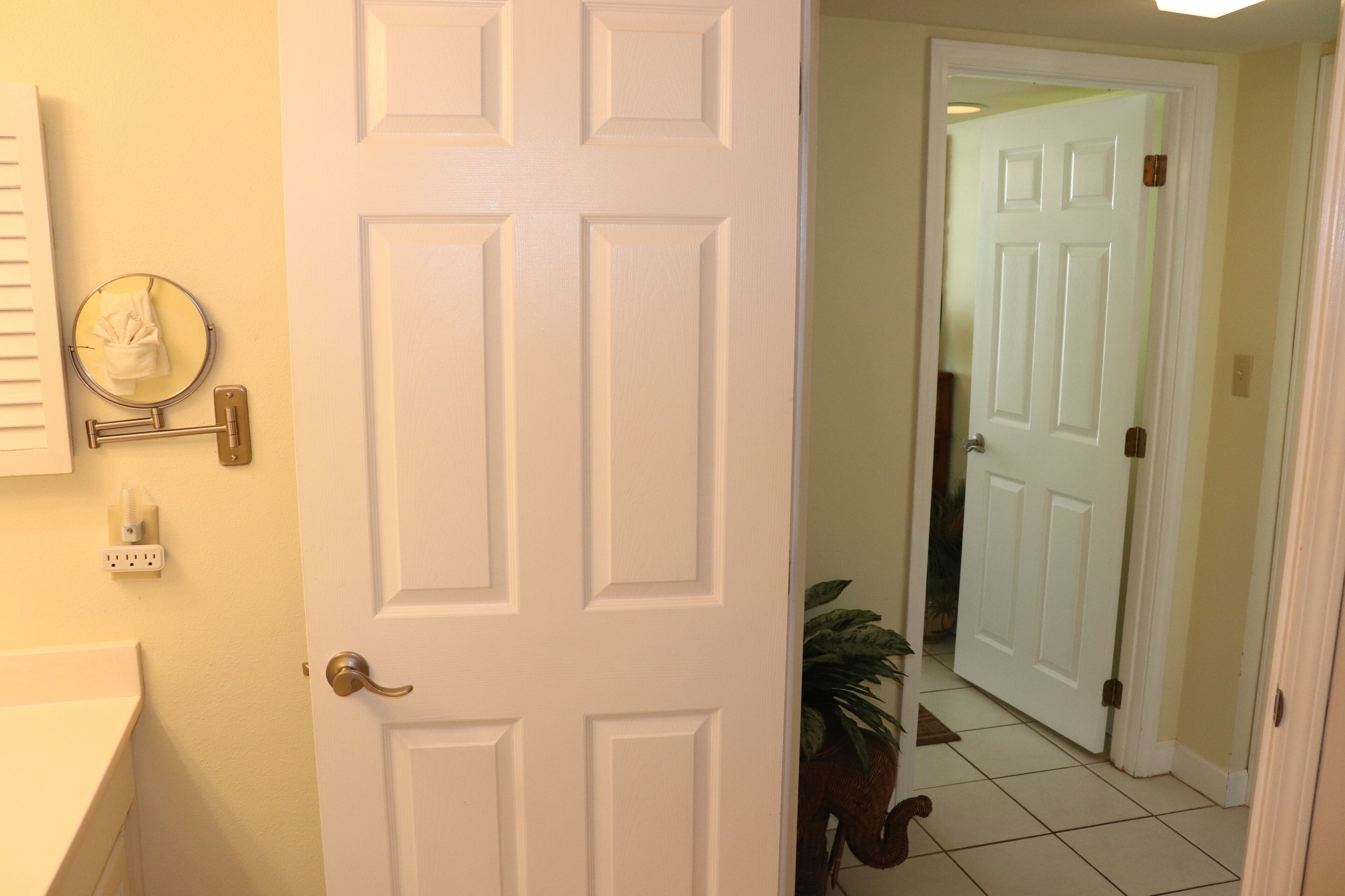 A white door with a brass handle, a mirror with a towel, and a power outlet on the wall.