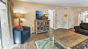 A living room with a blue sofa, a wooden coffee table, a cabinet, and a painting of a sunset over water. - two bedroom condo sleeps 7 persons (Gatlinburg)
