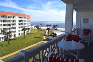 Un balcón con vistas al océano, un área de piscina y un edificio con varios balcones.