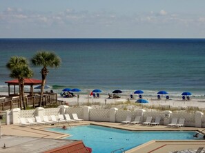 A pool area with lounge chairs and umbrellas, a beach in the background, and a clear view of the ocean.